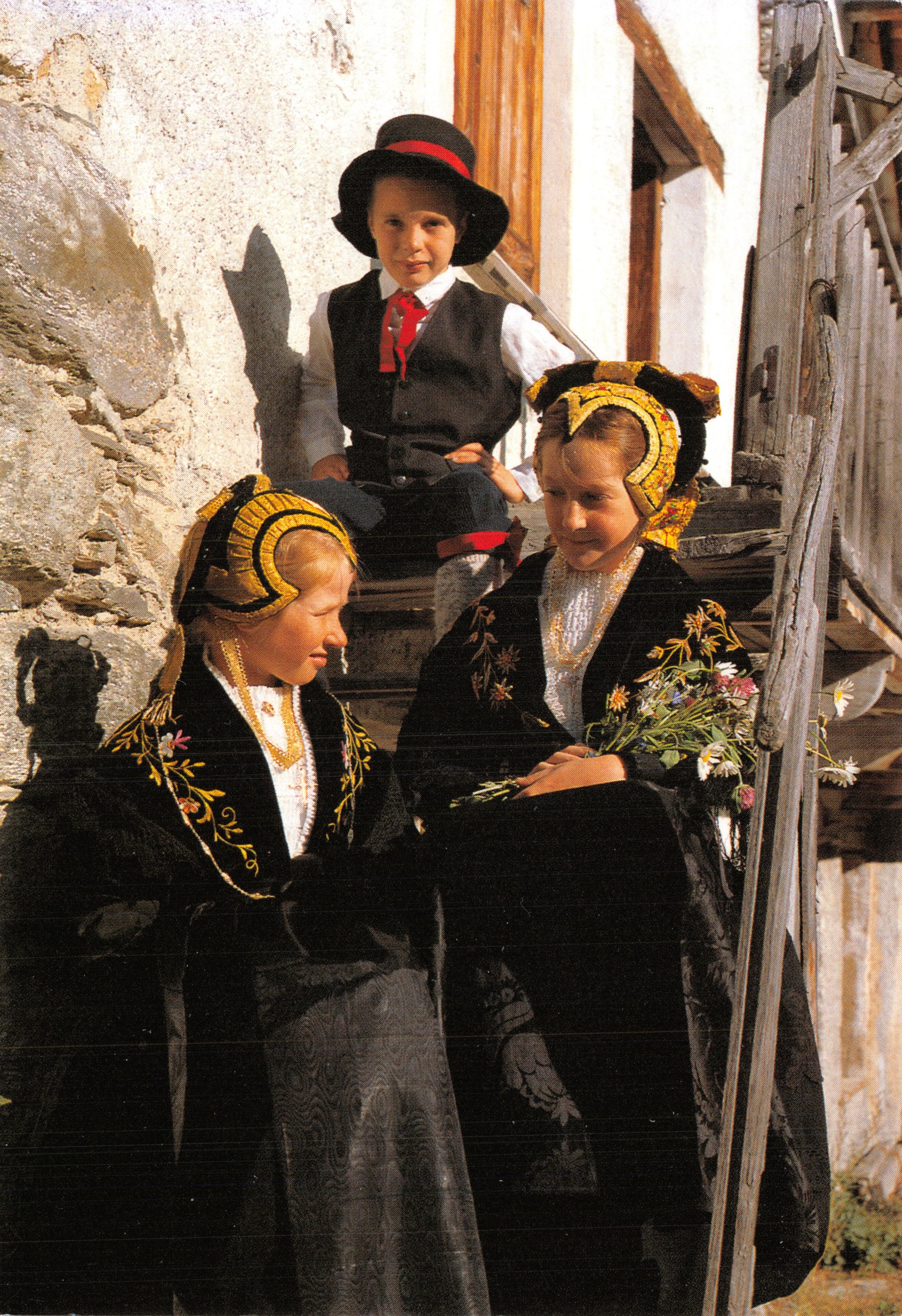 Traditional Savoy costumes — three children in folk costumes near a wooden staircase — Editions REVALP - ALBERTVILLE