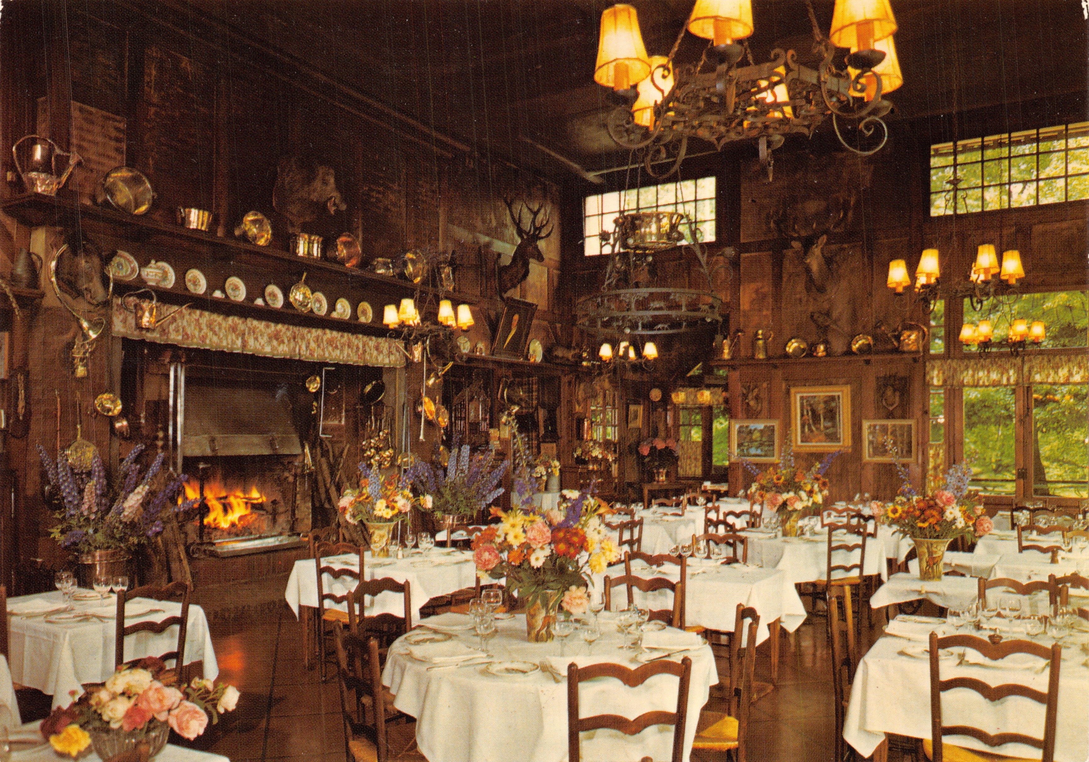 Sala de comedor de la Auberge du Grand-Veneur — interior rústico con chimenea y mesas puestas — editor L'PONCOLOR