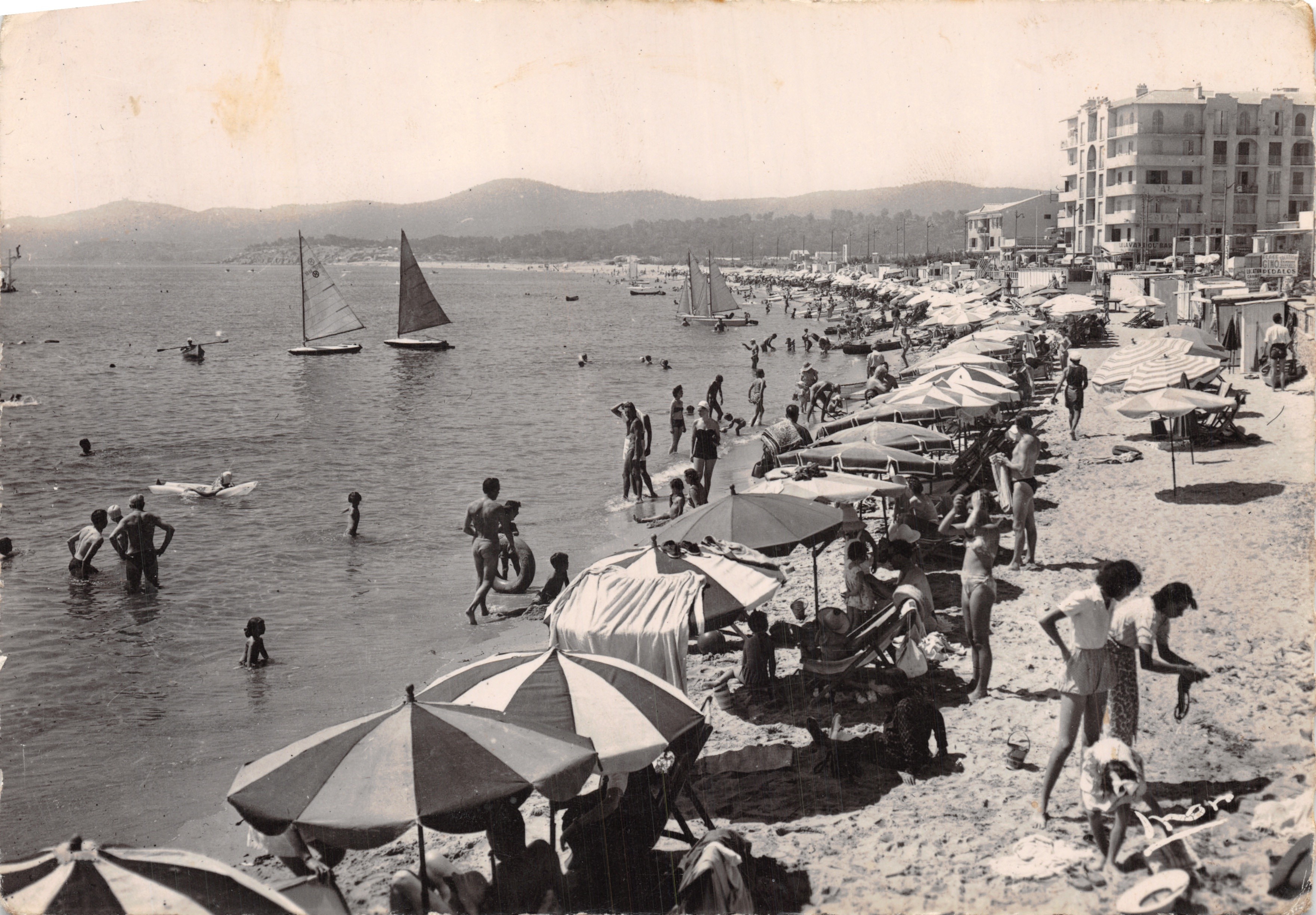 De strand van Le Lavandou — levendige uitzicht met zeilboten en zonneschermen — Éditions Les Editions Véritable