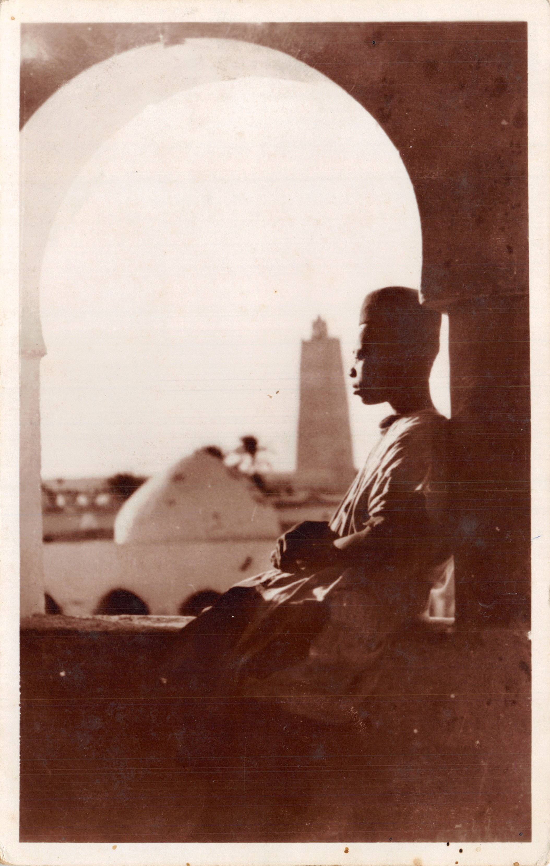 Man zittend in een boog — weergave van de moskee van de Koubba en de minaret van Alger — uitgave « La Cigogne »