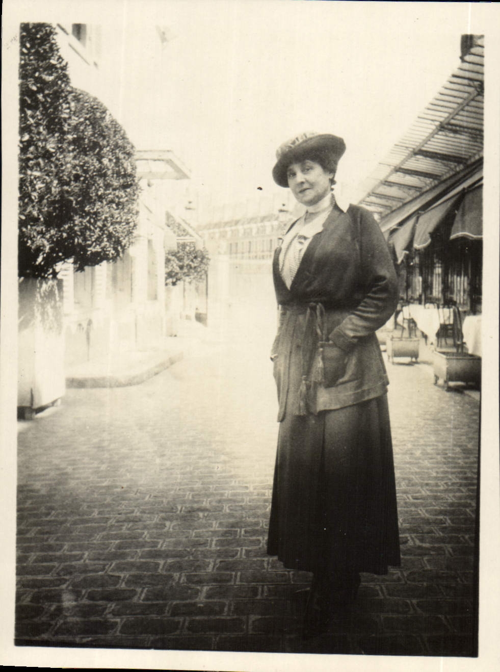 Femme en tenue d'époque — rue pavée avec arbres taillés — sans éditeur ni numéro visible