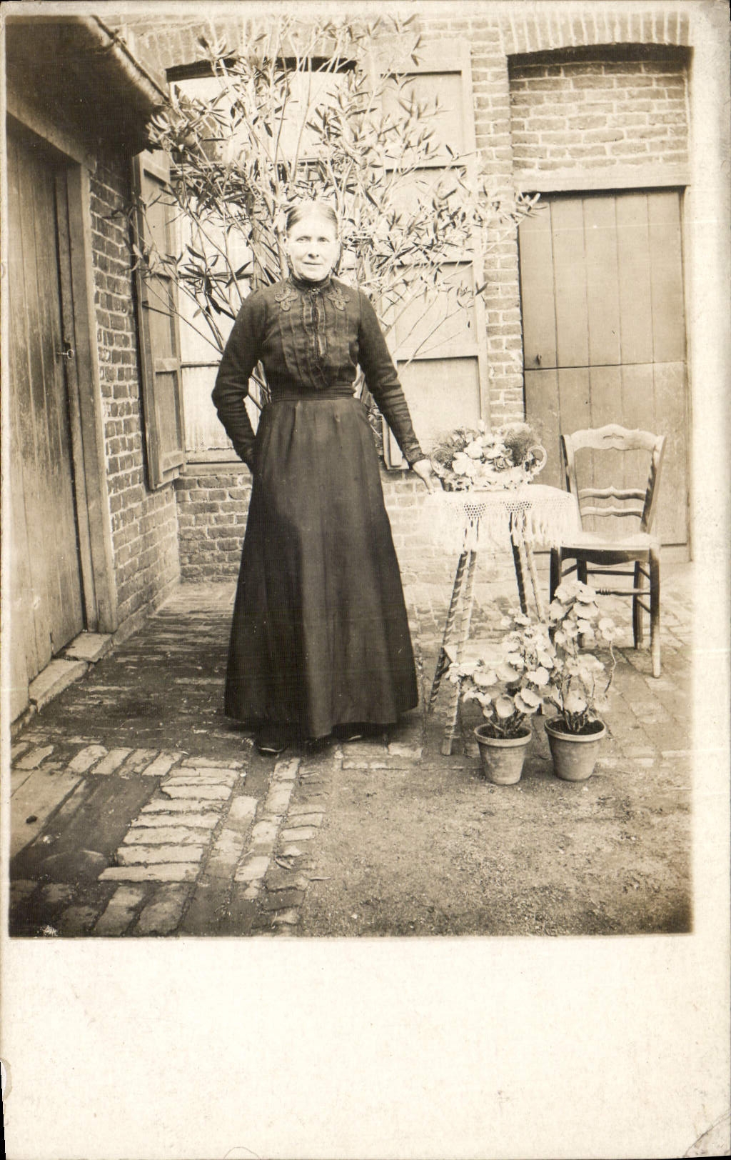 Femme en robe longue — devant une maison en briques — sans éditeur ni numéro visible