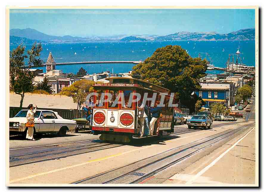 CPM Cable Car climbs a steep San Francisco hill as sailboats navigate the bay 
