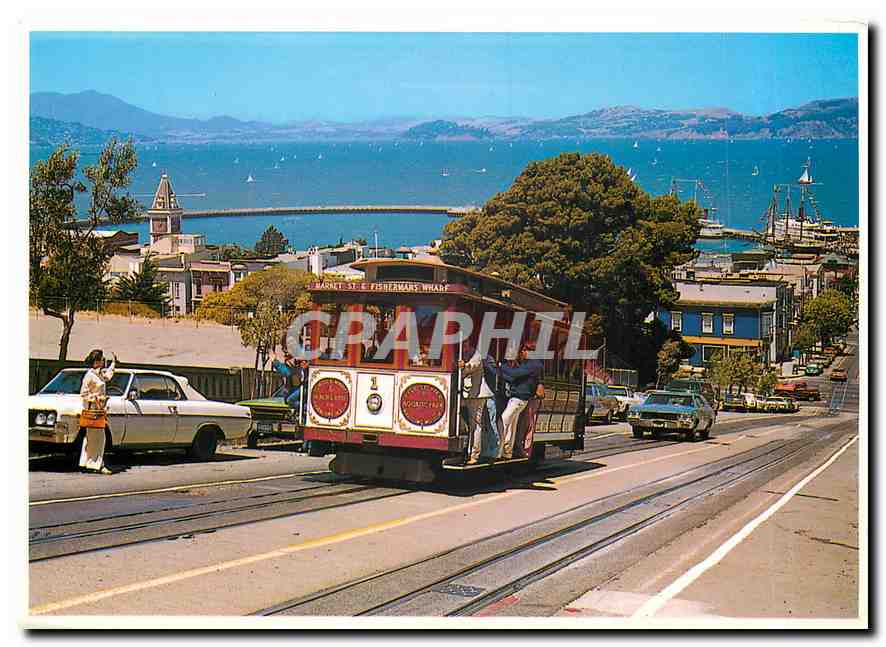 CPM Cable car climbs a steep San Francisco hill as sailboats navigate the bay 