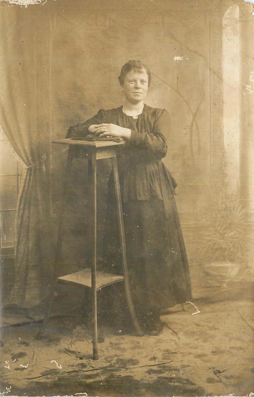 Femme en robe sombre — pose devant un meuble à deux niveaux — carte postale anonyme