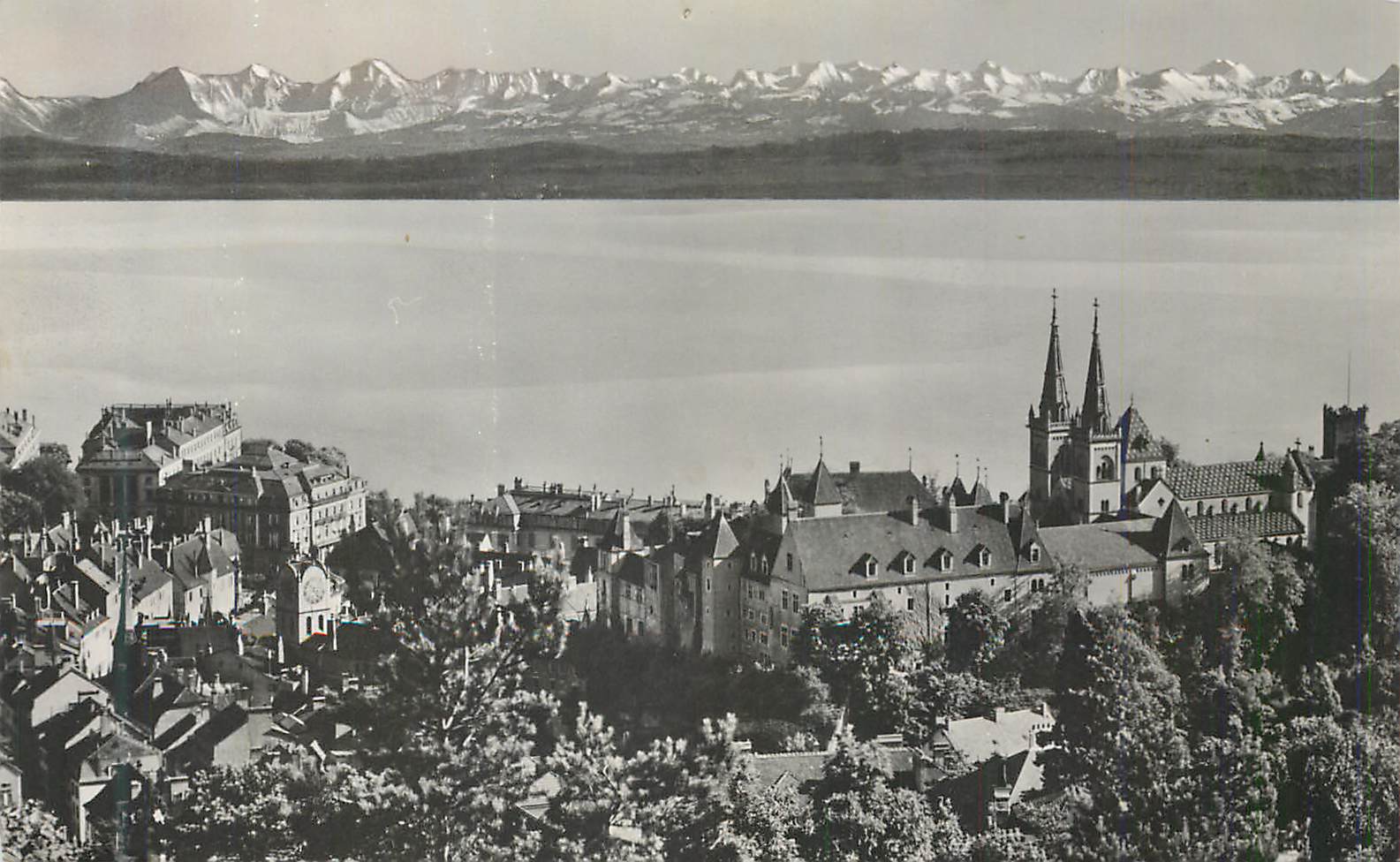 Aussicht auf die Stadt und den See mit schneebedeckten Bergen im Hintergrund — Verlag und Seriennummer nicht lesbar