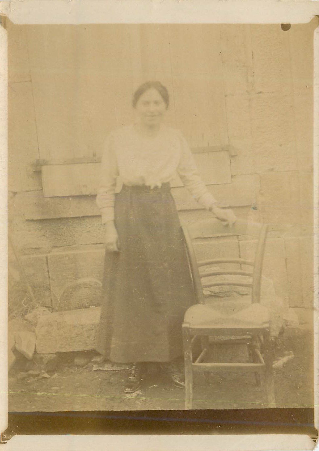 Femme en robe longue et chemise blanche — devant un mur en pierre et bois — sans éditeur ni numéro visible