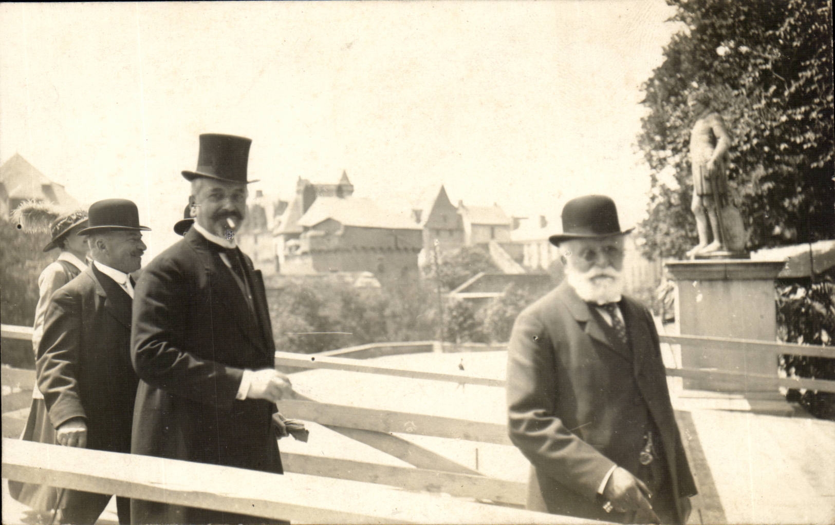 Groupe d'hommes en tenue formelle — vue de ville avec statue — éditeur CPAPHIL, n° de série non visible