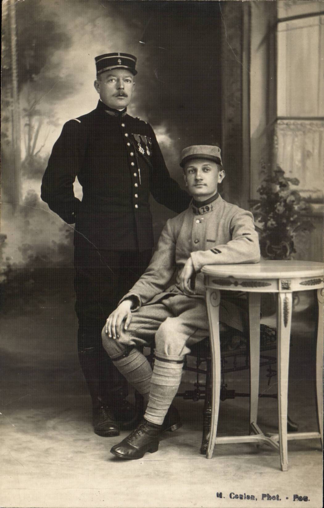 Due soldati — uno in uniforme scura, l'altro in divisa da campo — davanti a un decor di studio, fotografo U. Coulon, Fot. - Pec.