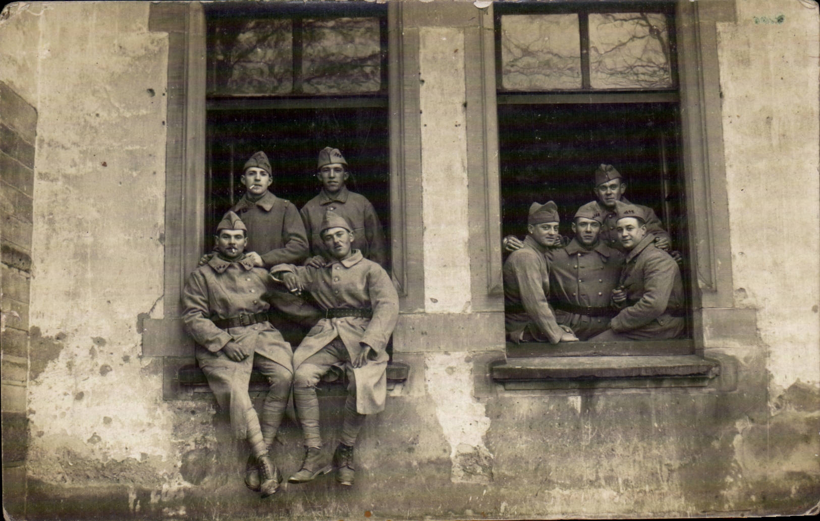Soldats en uniforme — posant dans des fenêtres d'un bâtiment — carte postale datée 1927