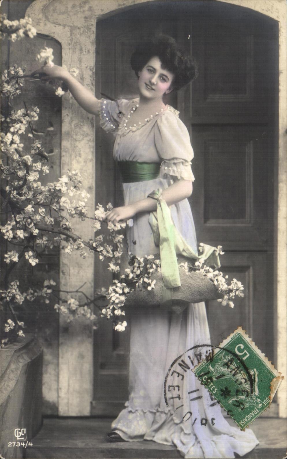 Young woman in a ruffled dress — in front of a gate with flowering branches — publisher C. L. C. n° 2734/4