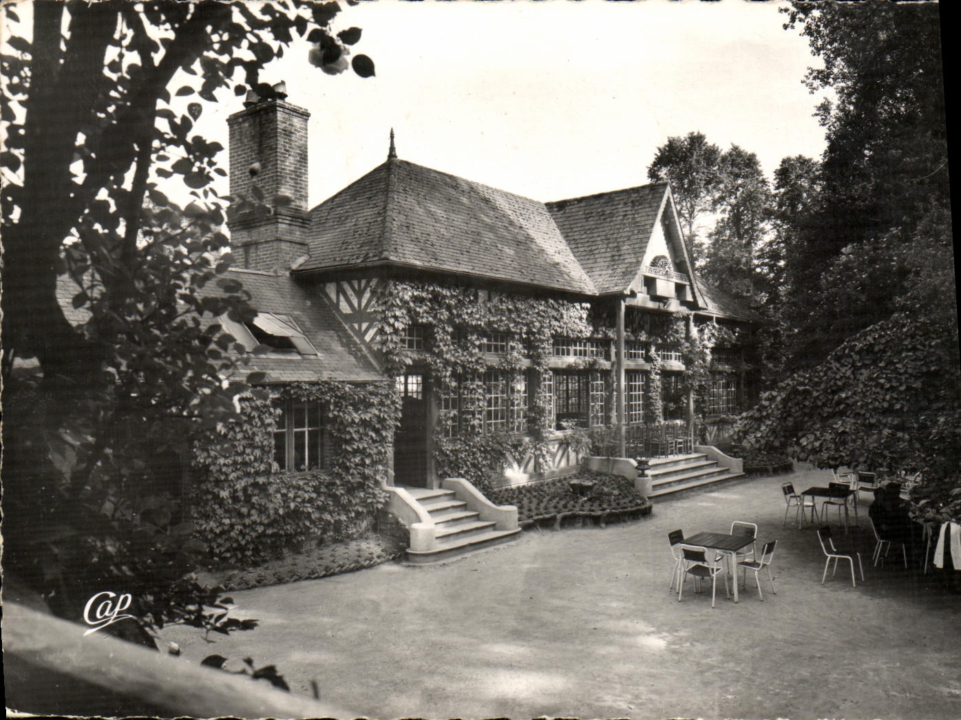 Maison en bois et pierre recouverte de lierre — jardin avec tables — éditeur Cap