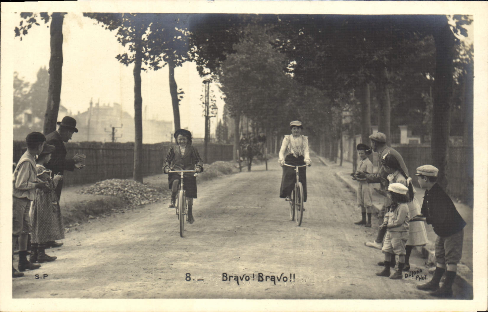 Deux cyclistes féminines — applaudies par un groupe d'enfants — photographiée par Dutong Phot.