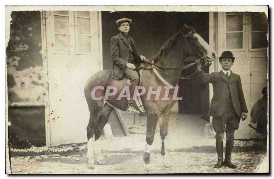 Jeune cavalier sur cheval — homme en costume tenant les rênes — devant une écurie