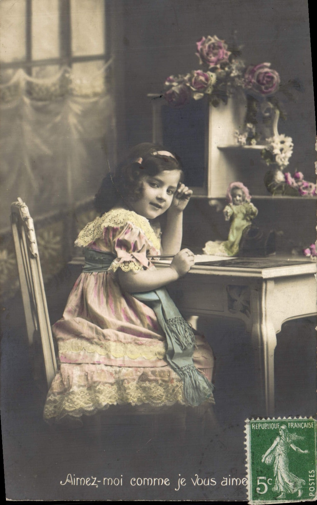 Petite fille assise à une table — texte imprimé 'Aimez-moi comme je vous aime' — éditeur inconnu, n° de série non visible