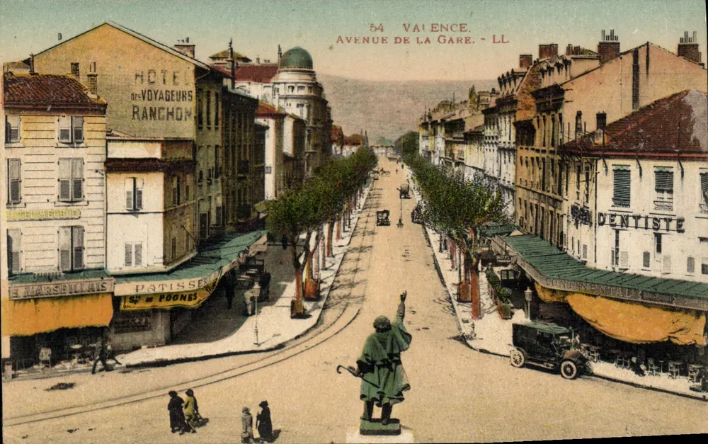 Avenida da Estação em Valence — LL, n°54 — vista de rua com estátua e comércios - Frente