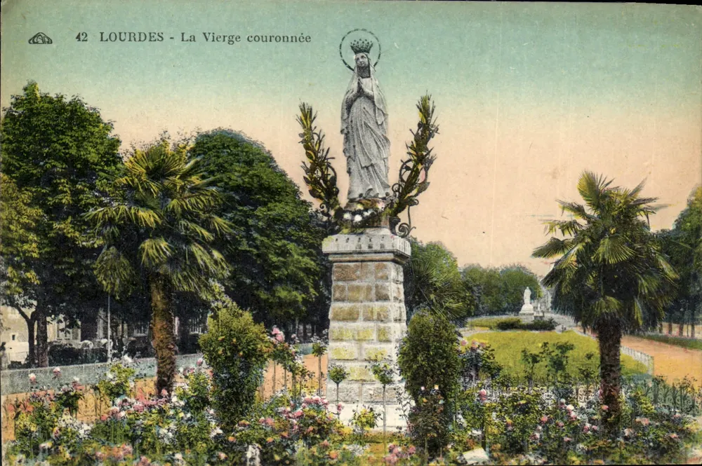 Lourdes - A Virgem coroada — estátua sobre pedestal de pedra, cercada de palmeiras e flores - Frente