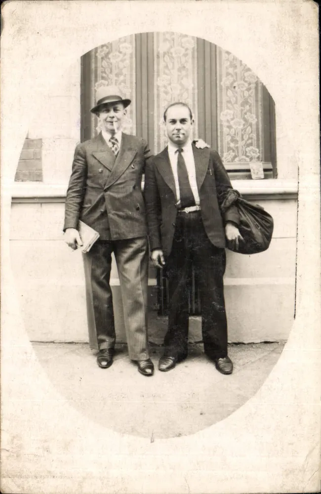 Dois homens em traje — diante de uma parede com janela decorada — carta postal - Frente
