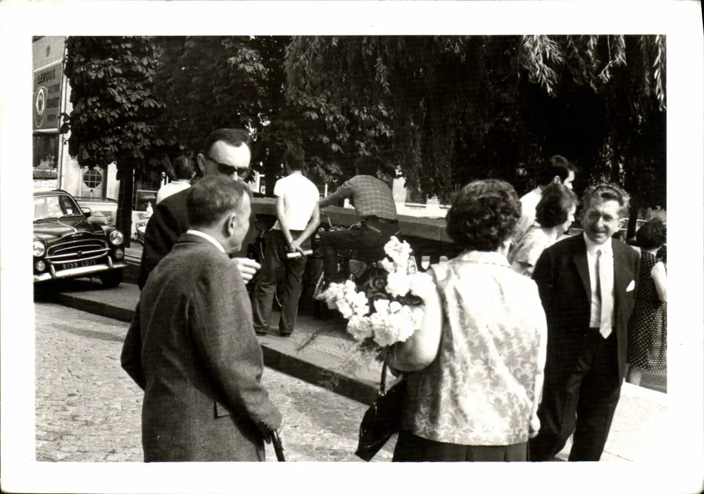 Groupe de personnes sur une place — devant une voiture Austin Healey 3000 - Recto