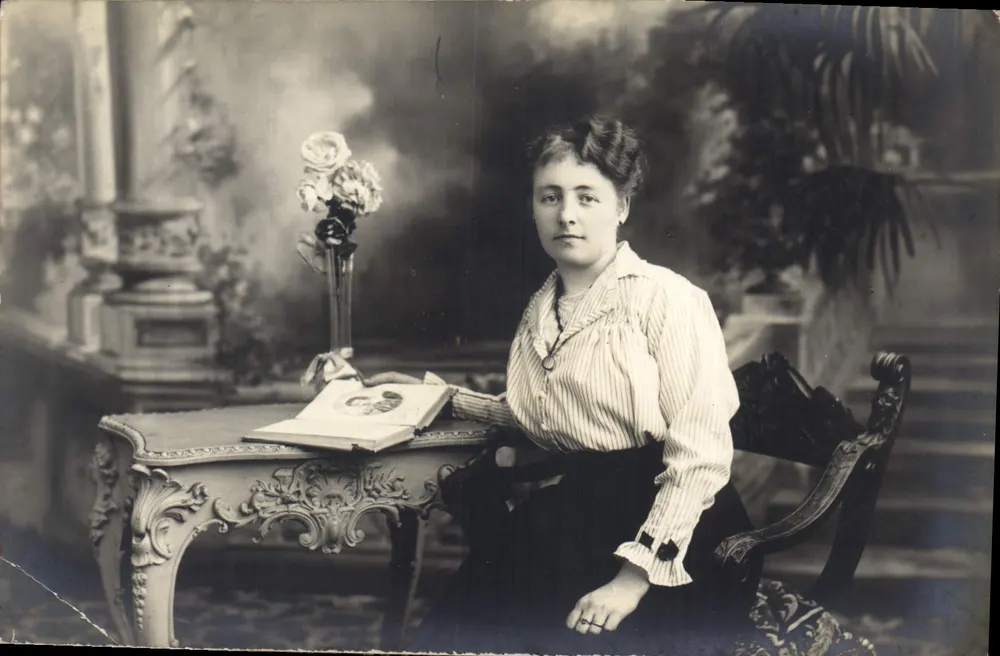 Mujer sentada a una mesa decorada — estudio fotográfico — sin editor ni número visible - Anverso