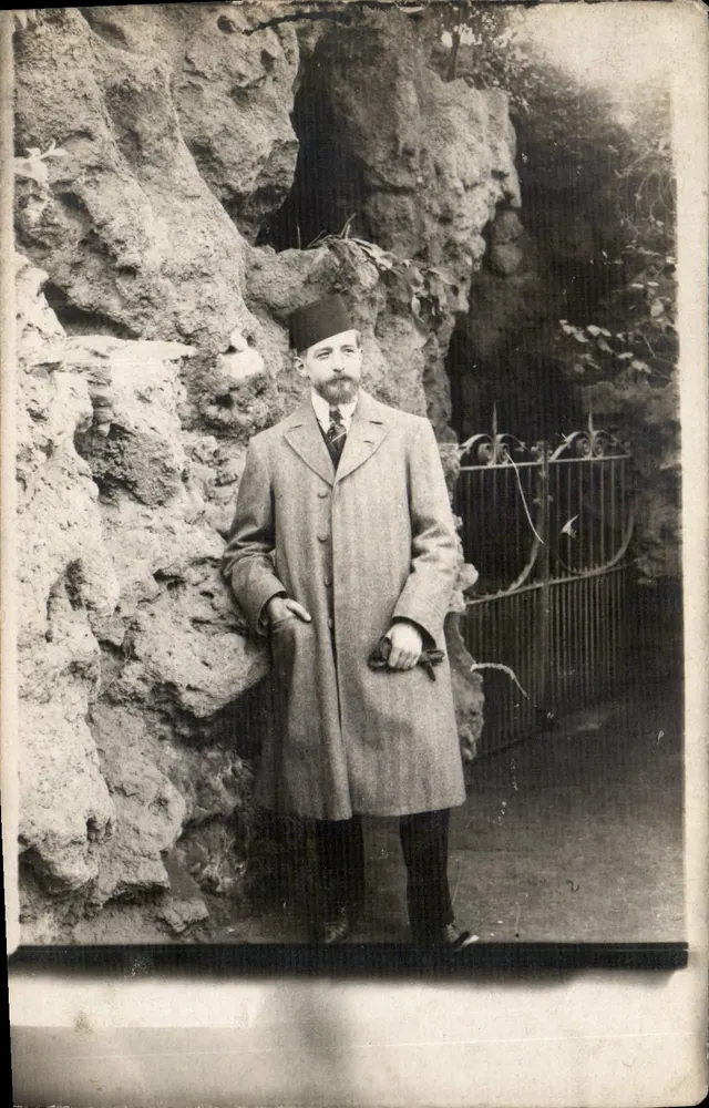Homme en manteau et fez — devant rochers et grille — Société des Produits F.L.E. - Recto