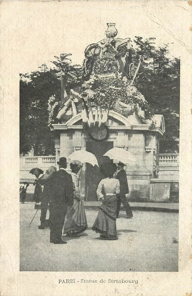 PARIS - Estátua de Strasbourg — monumento ornado de guirlandas e bandeiras, visitantes sob guarda-chuvas - Frente