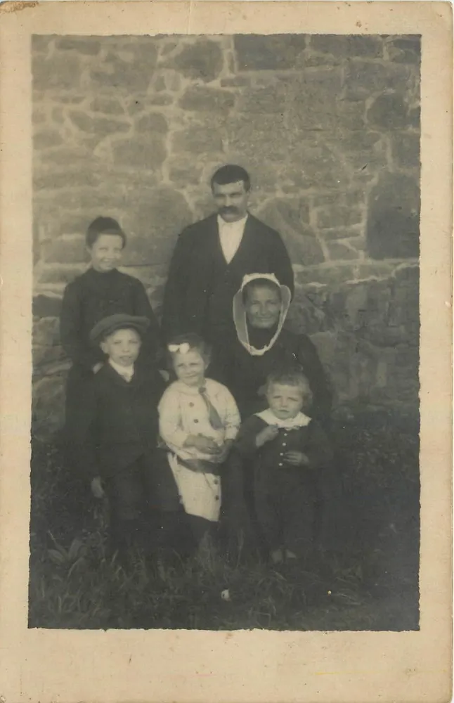 Família diante de muro de pedra — número de série não visível - Frente