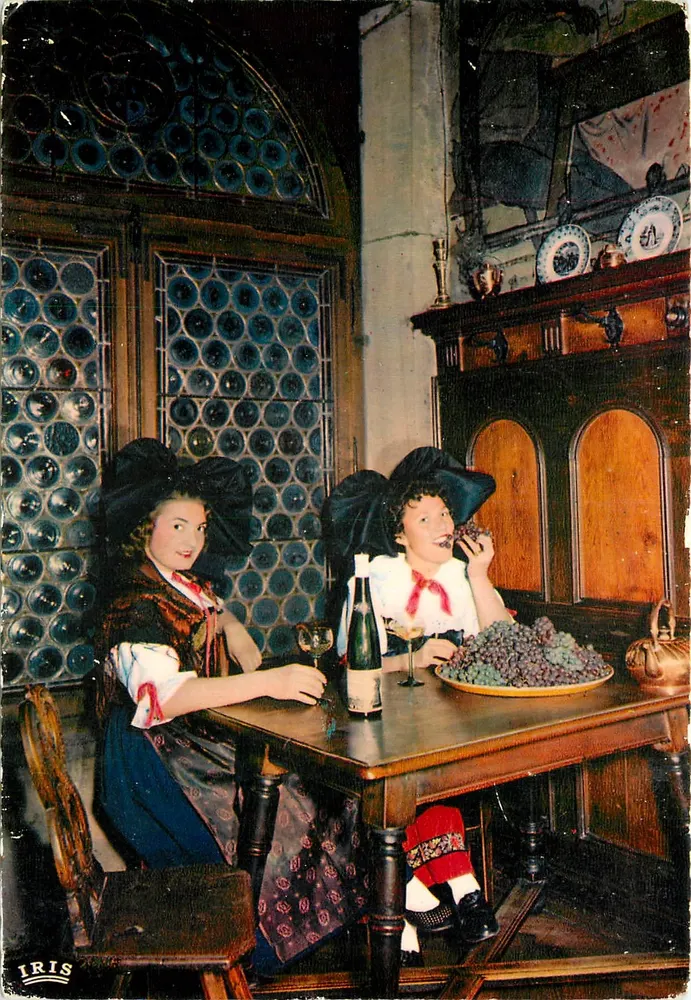 Dos mujeres en traje alsaciano — degustación de vino y uvas — editor IRIS, n° 67.567.78 - Anverso