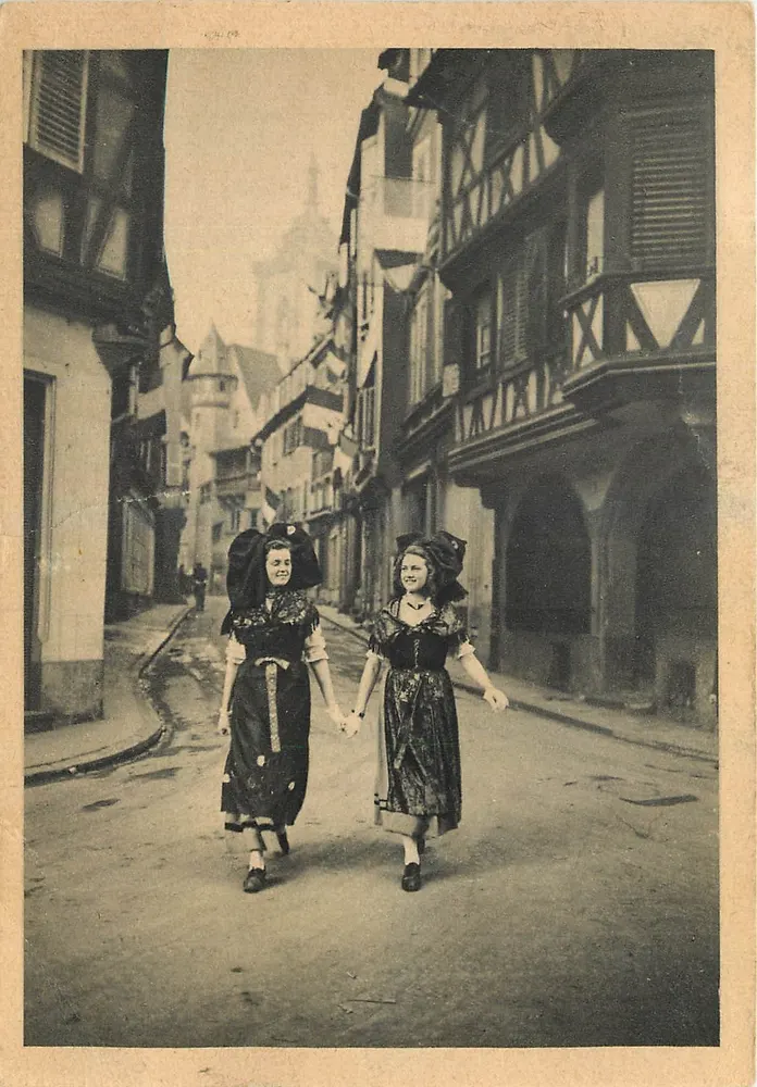 Deux jeunes femmes en costume traditionnel — rue pavée entre maisons à colombages — éditeur Première Gravure & Cie - Frente