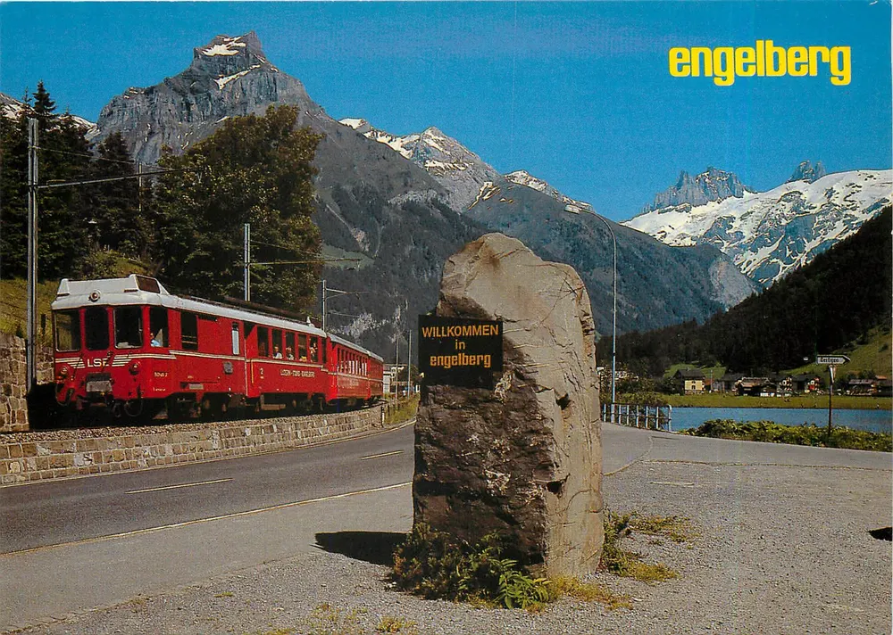 Engelberg — vista com trem vermelho e monumento de boas-vindas — Rud. Suter AG, n° 2061 - Frente