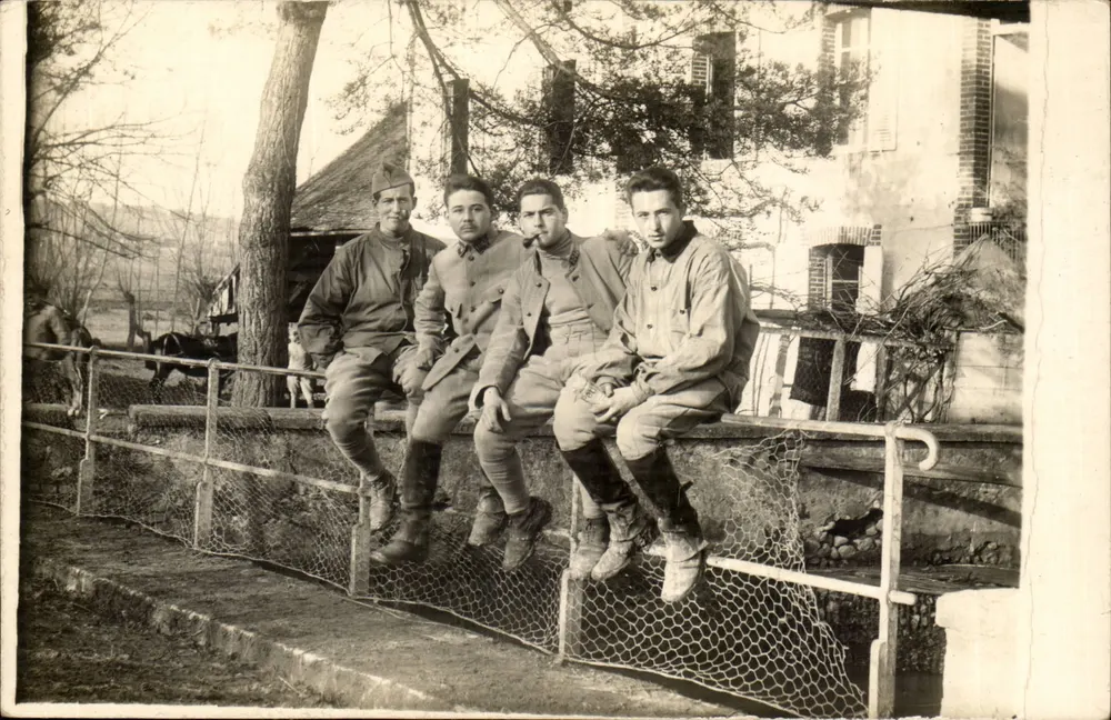 Vier Soldaten — in Felduniform — vor einem Eisenzaun — anonyme Ansichtskarte - Vorderseite