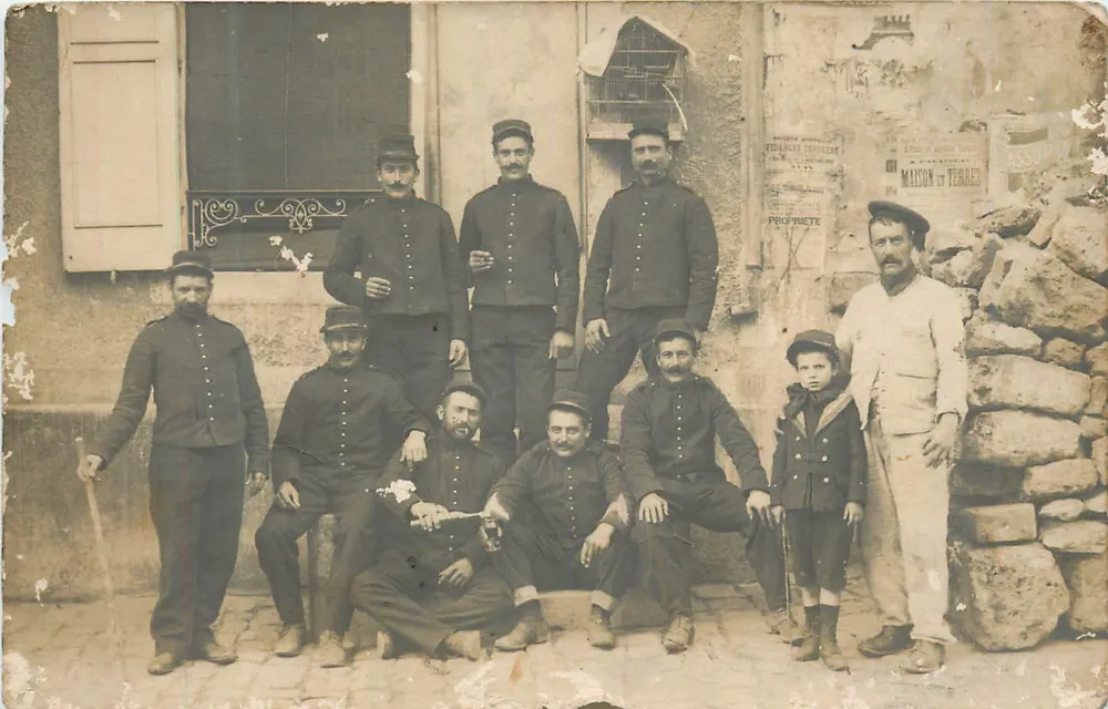 Groupe de soldats et un enfant — devant une façade avec affiches — éditeur 'MAISON DE TERRES' visible - Recto