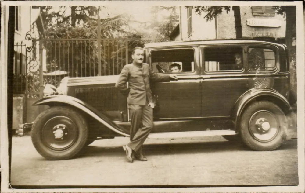 Homem e criança perto de um carro — diante de uma grade com letreiro 'LES FACQUETTES' — carta postal não editada - Frente