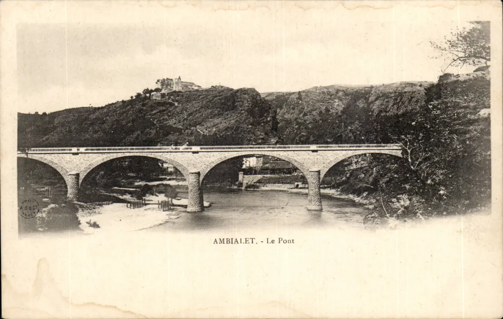 Ambialet - O Ponte — ponte de pedra sobre um rio, com edifício em colina no fundo - Frente