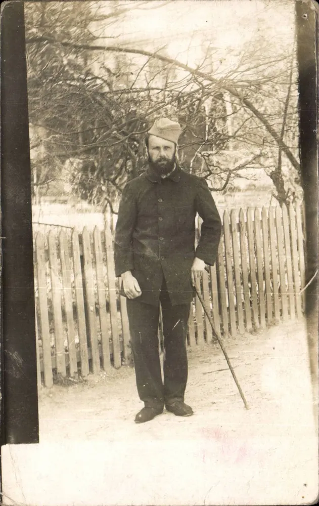 Homem em uniforme — diante de uma cerca de madeira — cartão postal datado 27 de março de 1915 - Frente
