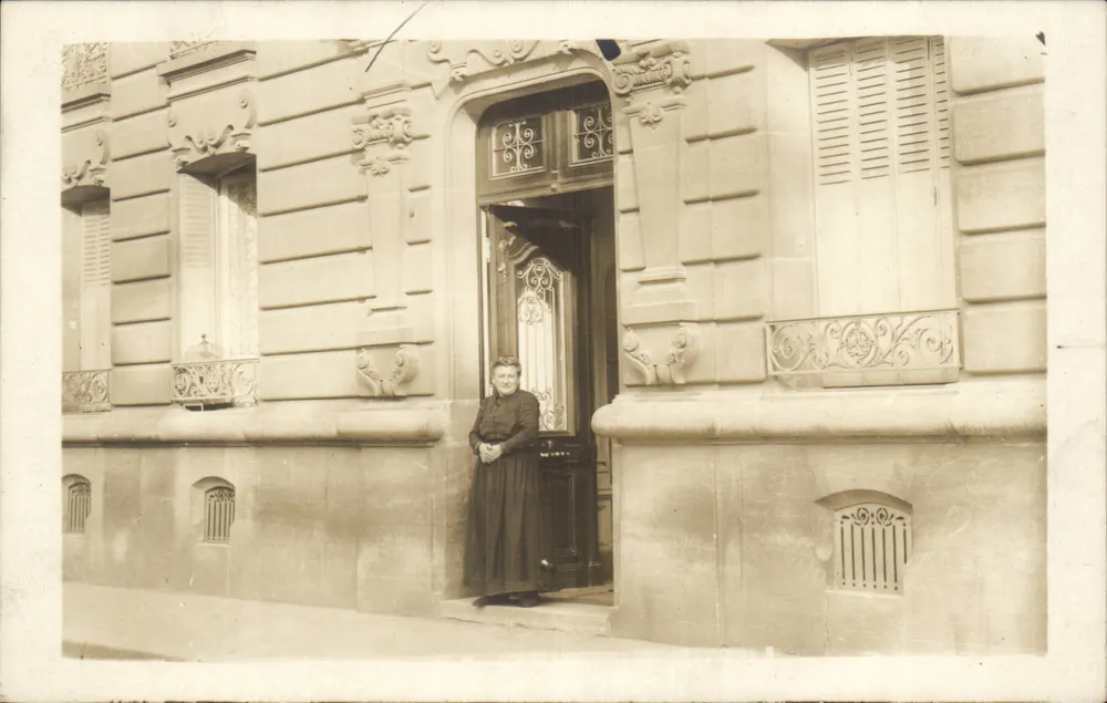 Donna davanti a una porta d'ingresso ornata — editore L. NOCH, Parigi - Recto