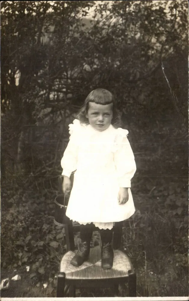 Menina pequena em vestido branco — sentada em uma cadeira em um jardim — Carta postal datada de 1919 - Frente