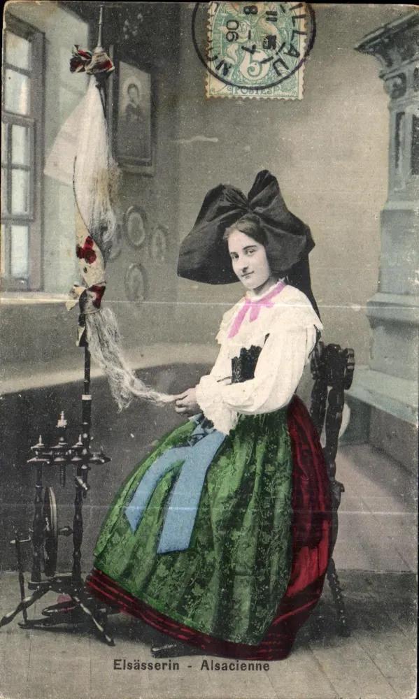 Alsacienne — mulher vestindo traje tradicional diante de uma máquina de fiar — editor não identificado, número de série não visível - Frente