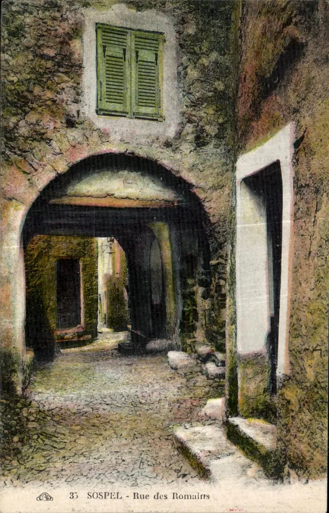 Sospel - Rue des Romairts — visão de um passagem com arco de pedra e janela com persianas verdes — n°35 - Frente