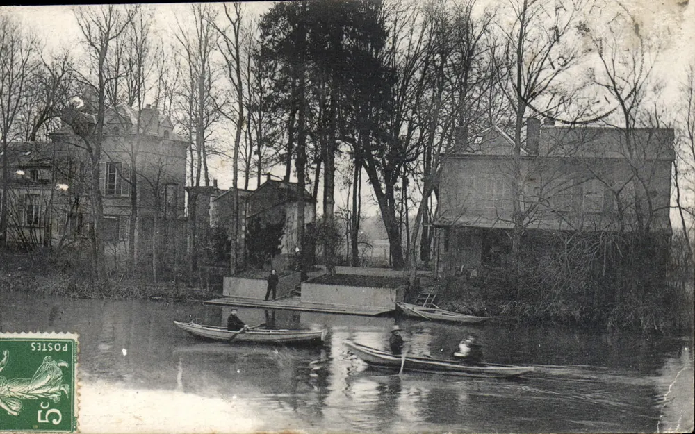 Scène fluviale — deux hommes en barque sur un canal bordé de maisons et d'arbres nus — éditeur non visible - Frente