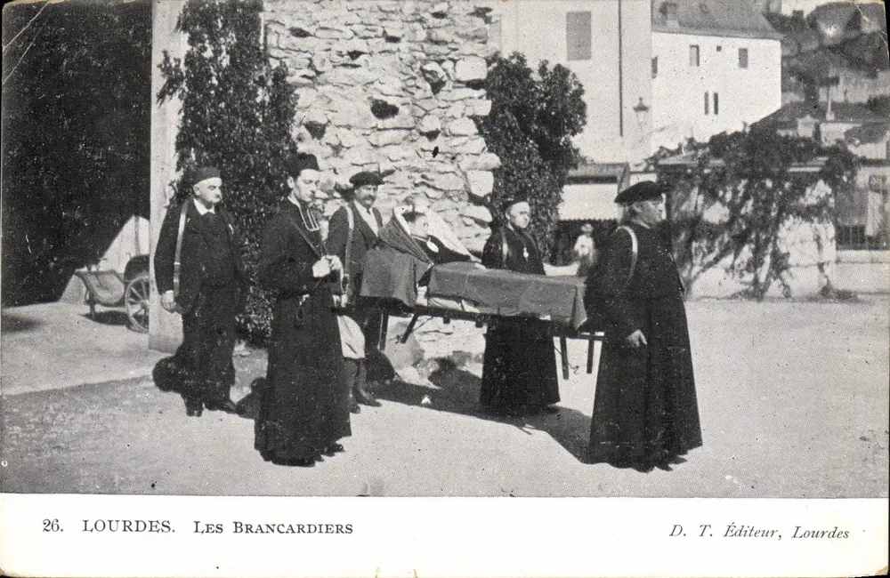 Lourdes. Les Brancardiers — scène de transport d'un blessé devant un mur de pierre, éditeur D. T. Éditeur, Lourdes, n° 26 - Frente