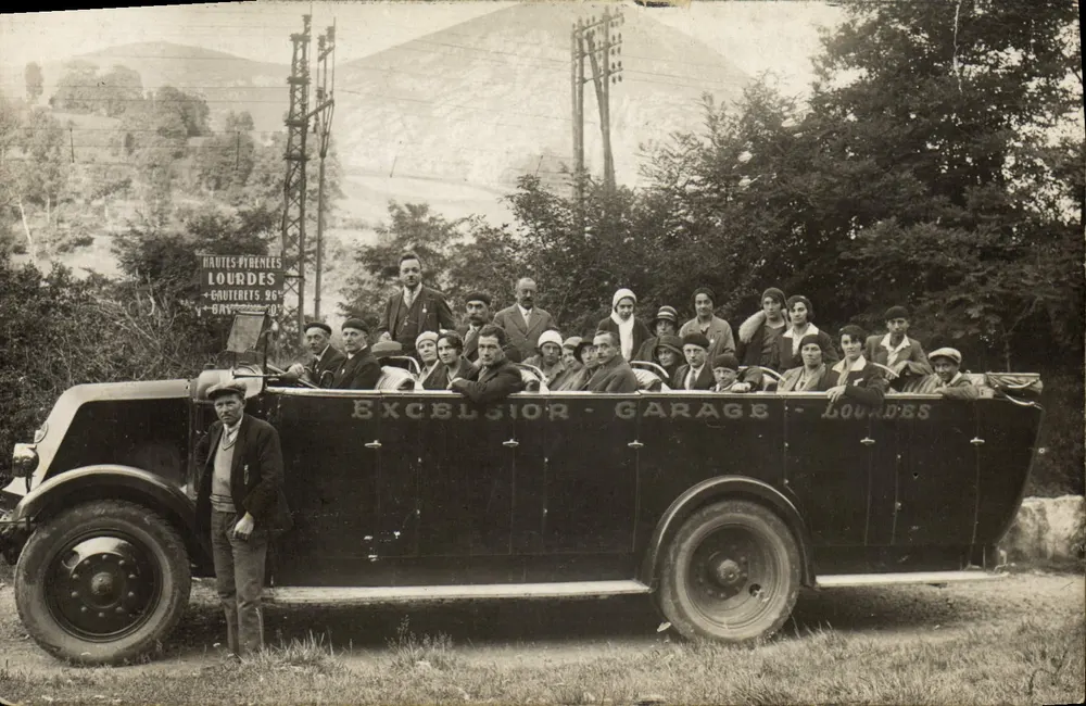 Gruppe von Personen in einem Excelsior - Garage - Lourdes-Laster — Straßenszene mit Schild 'HAUTES-PYRÉNÉES LOURDES - GAUTERETS 96' und Verlag 'EXCELSIOR - GARAGE - LOURDES' auf dem Fahrzeug - Vorderseite