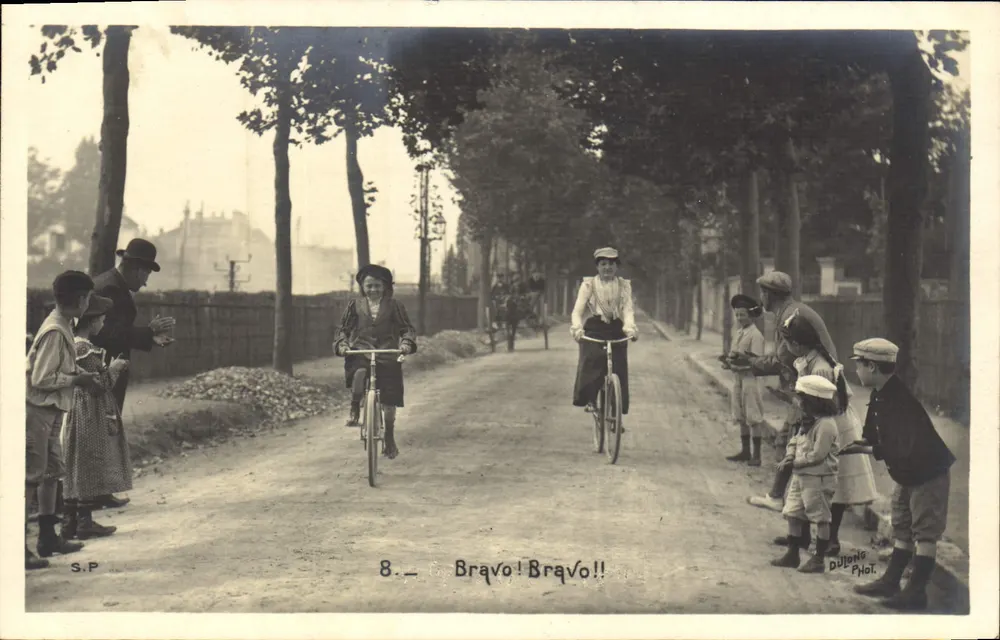 Due cicliste femminili — applaudite da un gruppo di bambini — fotografate da Dutong Phot. - Recto
