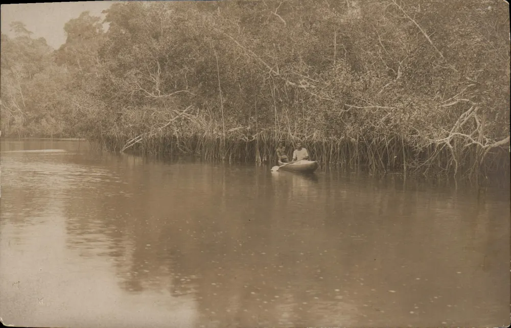 Zwei Männer in einem Kanu auf einem Fluss umgeben von Mangroven - Vorderseite