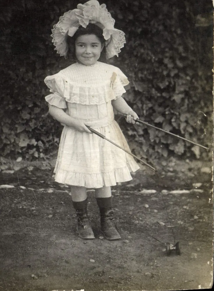 Menina em vestido branco e chapéu com babados — brincando com um brinquedo de corda — editor R. Desmoulins, n° 2356 - Frente