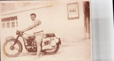 Homem em moto — em frente a um prédio com letreiro 'BAL' — sem editor ou número visíveis