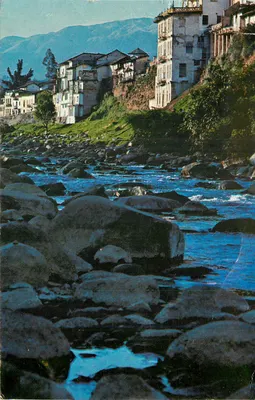 Vila à beira de um rio — montanhas no fundo — editor não identificável