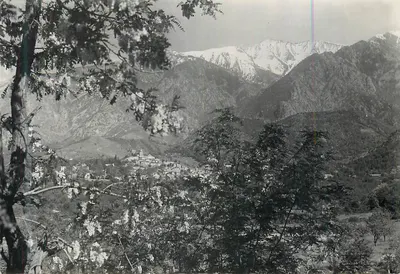 Vista panorâmica de um vilarejo encaixado — montanhas nevadas no fundo — editor não identificável