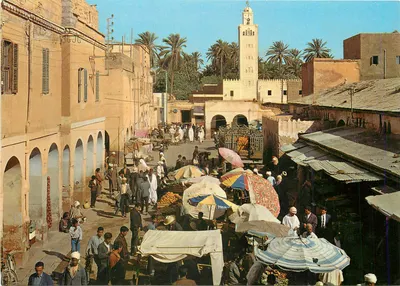 Mercado animado em Marrakech — torre da Koutoubia visível — editor não identificado