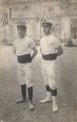 Dois jovens homens em traje esportivo — diante de um prédio decorado com bandeiras — editor Guillenniot, Scamillig & Cie, Paris